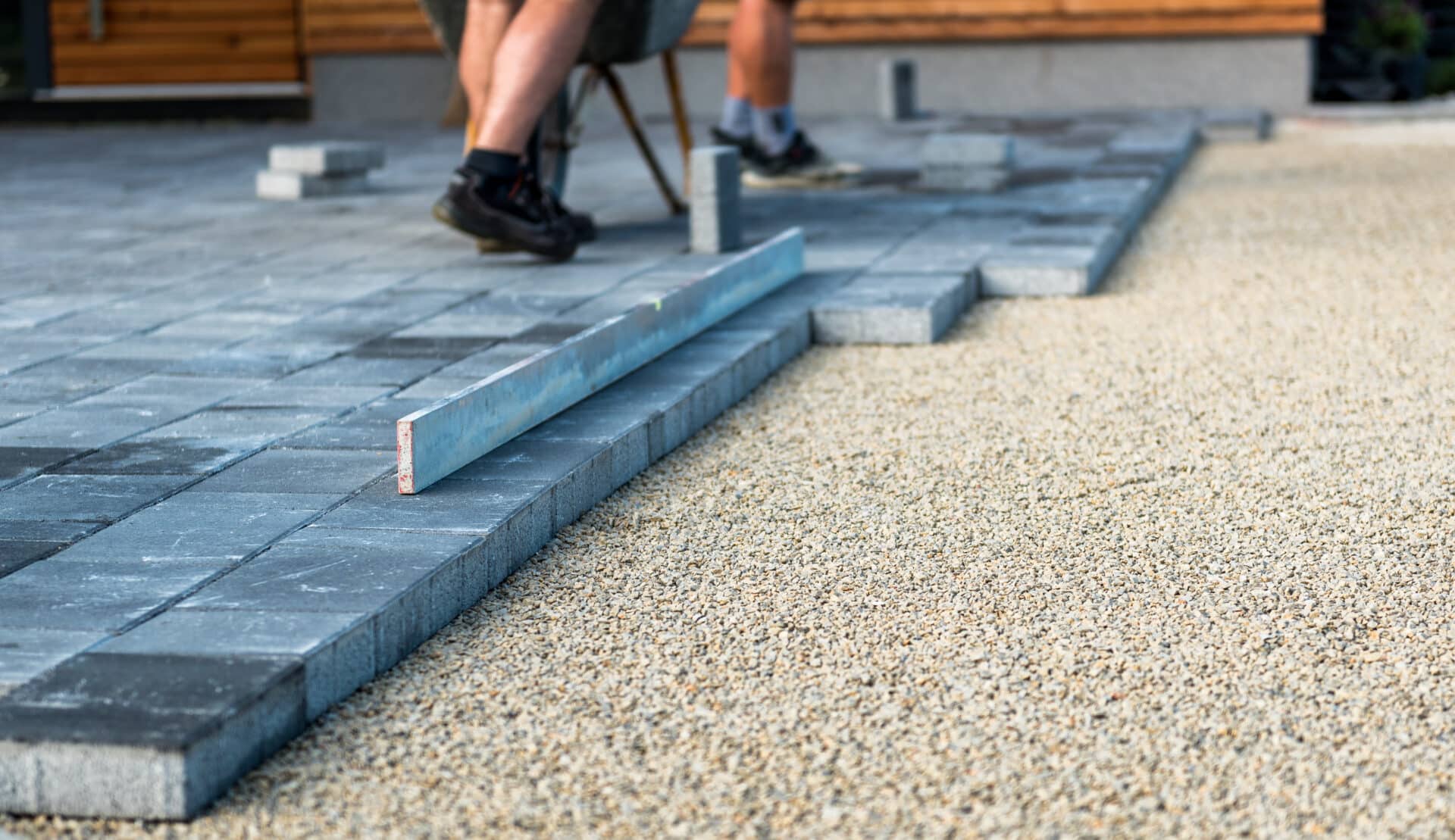 Laying gray concrete paving slabs in house courtyard driveway patio. Professional workers bricklayers are installing new tiles or slabs for driveway, sidewalk or patio on leveled foundation base made of sand at public or private residence.